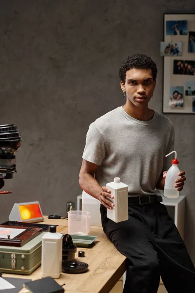 Hombre afroamericano enfocado midiendo cuidadosamente productos químicos de película fotográfica en un cuarto oscuro bien organizado - foto de stock
