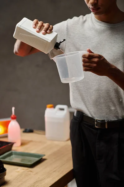 Beschnitten afrikanisch-amerikanischer mann gießt chemische lösung in messbecher, filmentwicklung — Stockfoto