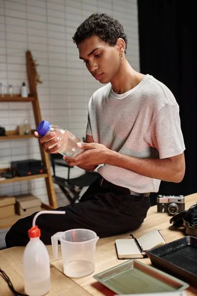 Bonito fotógrafo afro-americano segurando garrafa com solução química, desenvolvimento de filme — Fotografia de Stock