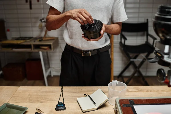 Homem afro-americano cultivado segurando recipiente de filme na câmara escura, passo no processo de desenvolvimento analógico — Fotografia de Stock
