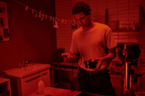 Photographe dans une pièce éclairée en rouge, l'homme noir gère soigneusement le développement du film avec minuterie de chambre noire — Photo de stock