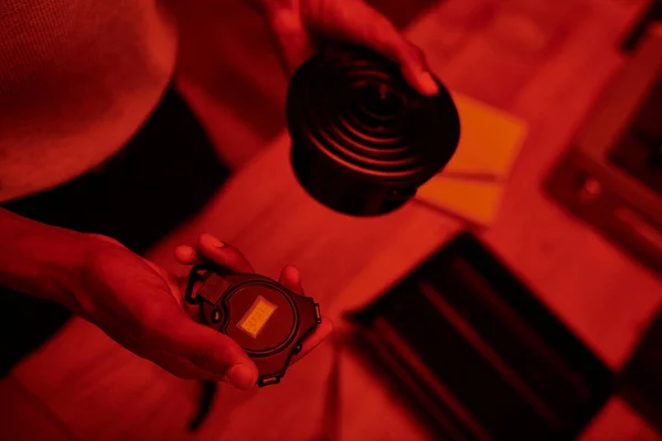 Photographe en chambre noire éclairée en rouge, vue de dessus de l'homme noir gère le développement du film avec minuterie chambre noire — Photo de stock
