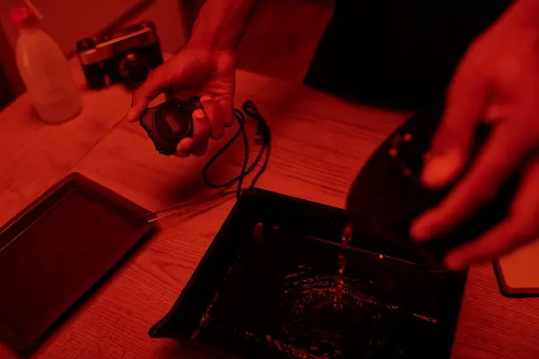 Fokus auf Timer in der Hand des Fotografen gießt Entwickler in Tablett zur Filmbearbeitung, rote Dunkelkammer — Stockfoto
