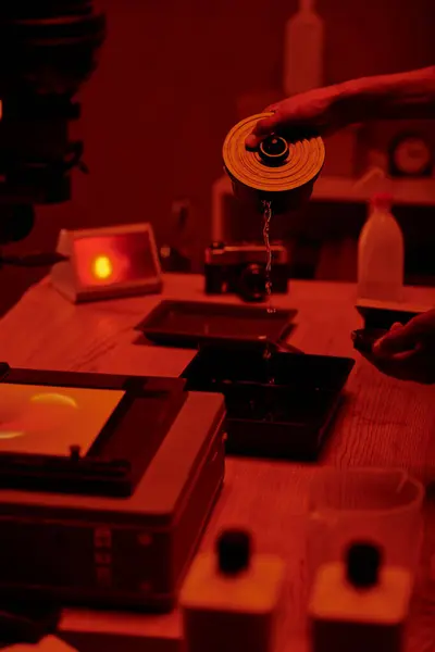 Ausgeschnittene Ansicht des Fotografen gießt Entwicklerflüssigkeit für die Filmverarbeitung, rote Dunkelkammer — Stockfoto