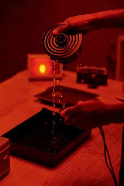 Cropped photo of photographer pouring developer liquid for film processing, red darkroom — Stock Photo