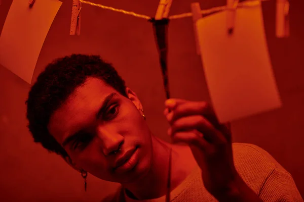 Молодий афроамериканський чоловік дивиться на свіжо розвинену стрічку в червоній темній кімнаті, ностальгія — стокове фото