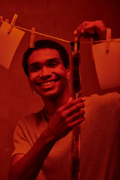 Щасливий афроамериканський чоловік вішає свіжо розвинену стрічку в червоно-світлій темній кімнаті, ностальгії — стокове фото
