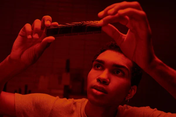 Сфокусированный африканский американский фотограф рассматривает разработанную ленту в красной фотолаборатории — стоковое фото