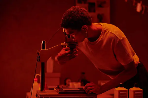 A meticulous photographer inspecting photo negative under the red safety light of a darkroom — Stock Photo