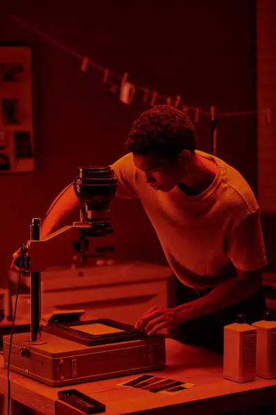 African american photographer inspecting photo negative under the red safety light of a darkroom — Stock Photo