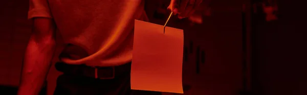 Bannière recadrée du photographe tenant des pinces à épiler avec du papier photo dans une chambre noire avec lumière rouge — Photo de stock