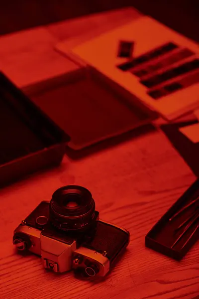 Черный стол с аналоговой камерой и инструментами для разработки пленки под светом красного света — стоковое фото