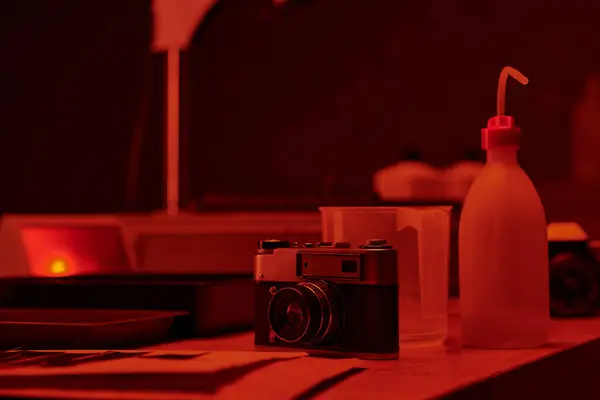 Table with analog camera and different tools for film development in darkroom with red light — Stock Photo