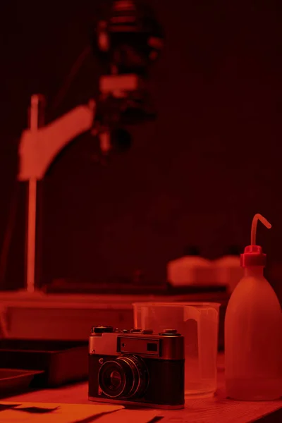 Аналогова камера та різні інструменти для розробки плівки на столі в темній кімнаті з червоним світлом — стокове фото