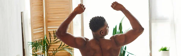 Back view of muscular shirtless african american man stretching in modern bedroom, horizontal banner — Stock Photo