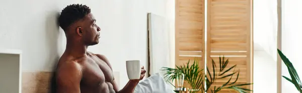 Pensive shirtless african american man with coffee cup sitting and looking away in bedroom, banner — Stock Photo