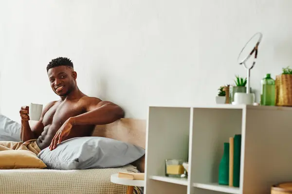 Cheerful shirtless african american man with coffee cup looking away on cozy bed at home, morning — Stock Photo