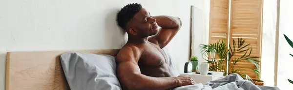 Junger afrikanisch-amerikanischer Mann mit geschlossenen Augen und muskulösem Oberkörper auf Bett sitzend und streckend, Banner — Stockfoto