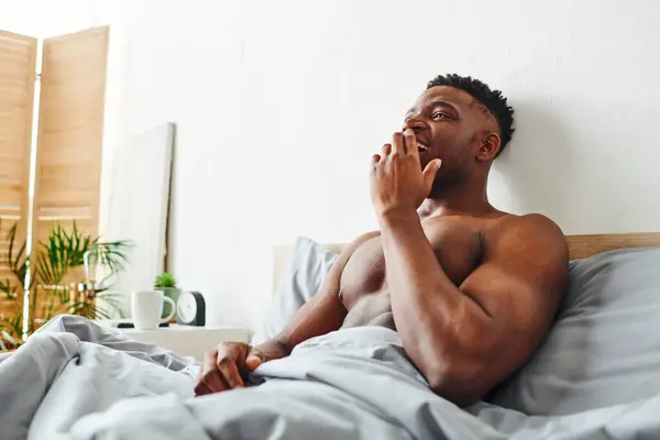 Happy shirtless african american man with strong body waking up and yawning on bed in morning — Stock Photo