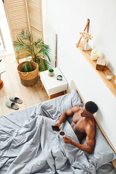Vista superior do homem afro-americano bonito com café da manhã e smartphone na cama acolhedora em casa — Fotografia de Stock