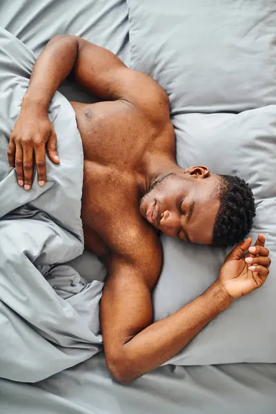 Vista superior de joven afroamericano hombre durmiendo en cómoda cama bajo suave manta en la mañana - foto de stock