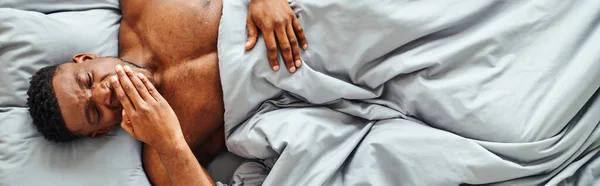 Top view of dreamy african american guy yawning and waking up on cozy bed at home, horizontal banner — Stock Photo