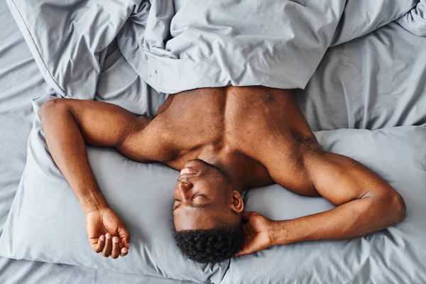 Von oben: Afrikanisch-amerikanischer Mann mit kräftigem Körper träumt von grauer Bettwäsche zu Hause — Stockfoto