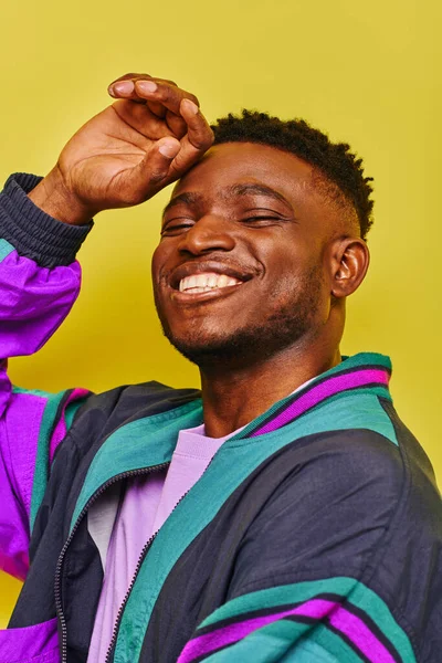 Fashionable african american man in windbreaker jacket posing and laughing at camera on yellow — Stock Photo