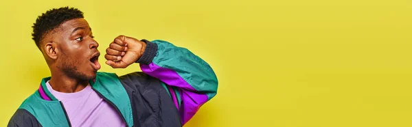 Amazed trendy african american man in stylish windbreaker jacket looking away on yellow, banner — Stock Photo