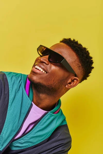 Ritratto di felice uomo afroamericano in occhiali da sole e giacca luminosa distogliendo lo sguardo sul giallo — Foto stock