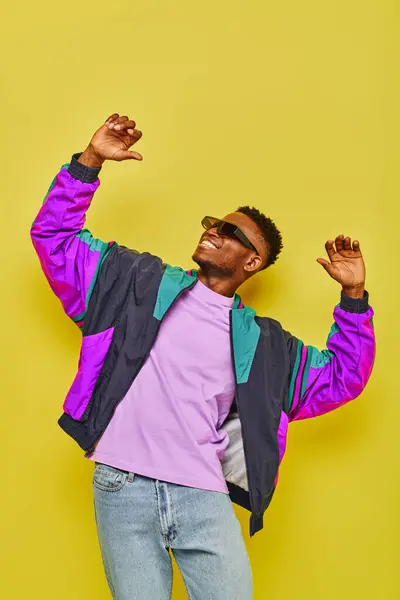 Happy african american man in stylish casual attire and sunglasses dancing on yellow backdrop — Stock Photo