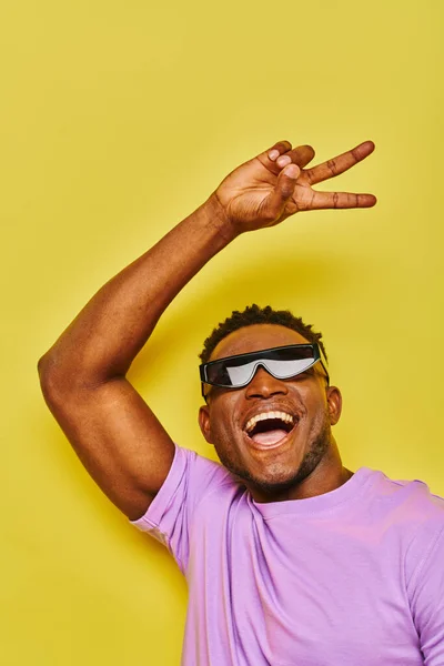Overjoyed stylish african american man in sunglasses showing victory sign and screaming on yellow — Stock Photo