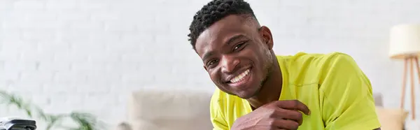 Retrato de hombre americano africano deportivo y alegre mirando la cámara en la sala de estar, pancarta - foto de stock