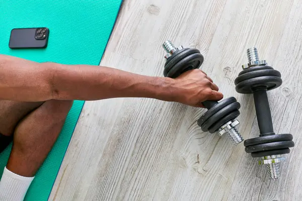 Cropped view of athletic african american man sitting on fitness mat and taking dumbbell, top view — Stock Photo