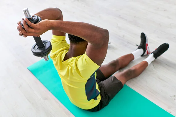 Afrikanisch-amerikanischer Mann in Sportbekleidung sitzt auf Fitnessmatte und trainiert mit Hantel, Blick hoch — Stockfoto