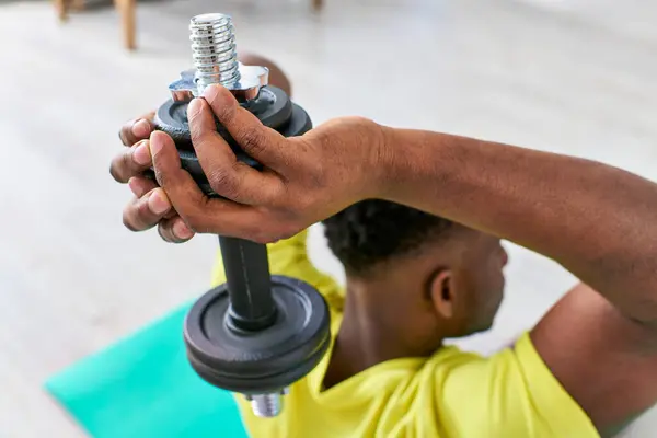 Selective focus of dumbbell in hands of african american man training in living room, home workout — Stock Photo