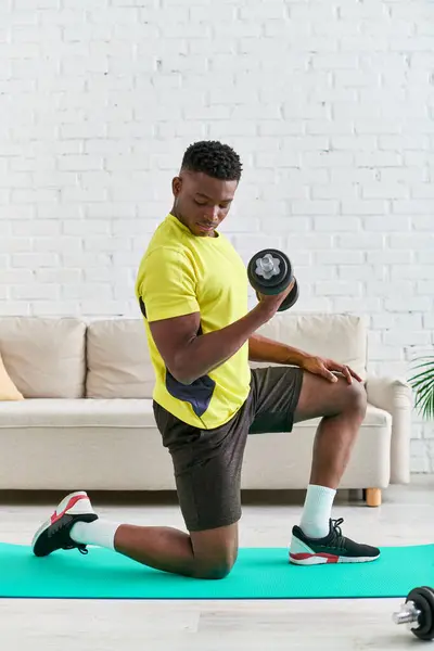 Молодий афроамериканський чоловік в стильному спортивному одязі тренування з гантелі фітнес килимок вдома — стокове фото