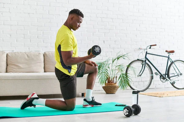 Atlético afro-americano cara no elegante sportswear formação com haltere de fitness mat em casa — Fotografia de Stock
