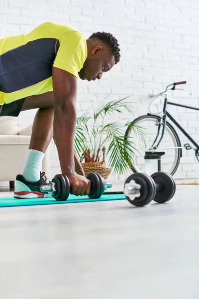 Chico afroamericano joven y fuerte en ropa deportiva con estilo ejercicio con mancuerna de la estera de fitness - foto de stock