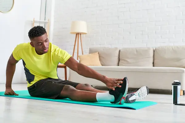 Joven afroamericano chico sentado y estiramiento en el hombre de fitness en sala de estar, entrenamiento en casa - foto de stock