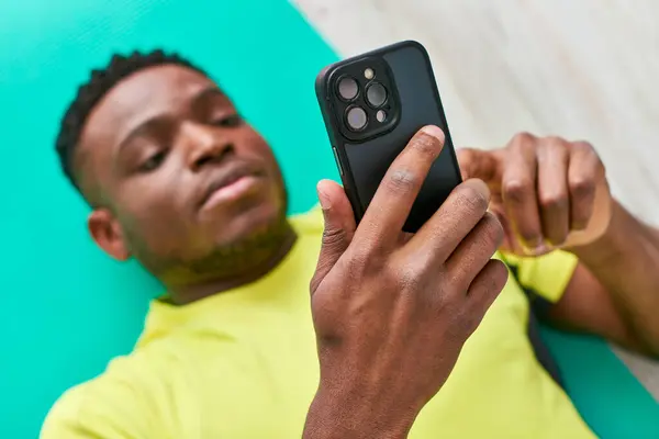 Vista de ángulo alto del atlético afroamericano hombre en ropa deportiva navegación por Internet en el teléfono inteligente - foto de stock