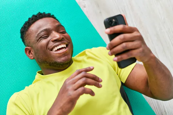 Young cheerful african american man in sportswear browsing internet on smartphone, top view — Stock Photo