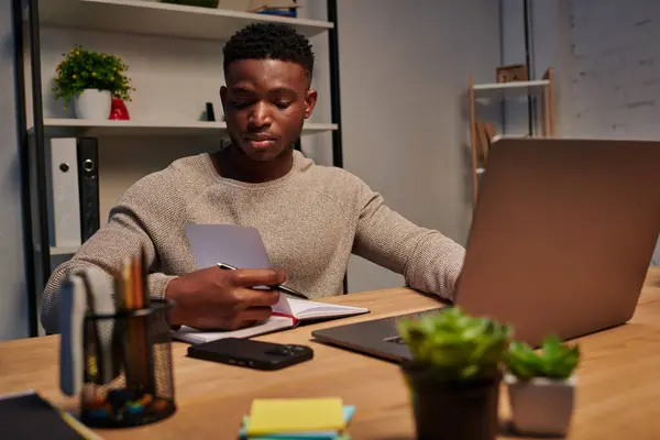 Giovane uomo afroamericano con computer portatile e notebook che lavora in ufficio a casa di notte, libero professionista — Foto stock