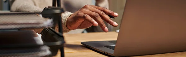 Vista recortada del joven afroamericano freelancer que trabaja en el ordenador portátil por la noche en casa, pancarta - foto de stock