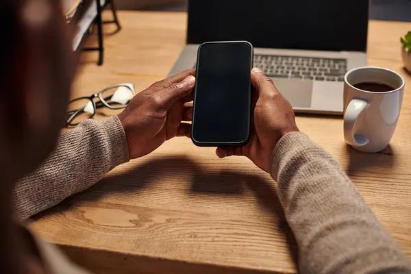 Hombre americano africano alegre que habla en smartphone y que escribe en el cuaderno mientras que trabaja de hogar - foto de stock