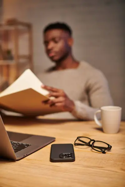 Selective focus on eyeglasses and laptop with smartphone near blurred african american freelancer — Stock Photo