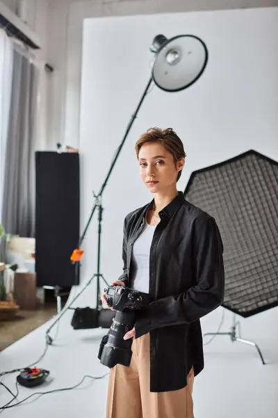 Attrayant à poil court photographe femme en tenue décontractée regardant la caméra tandis que dans son studio — Photo de stock