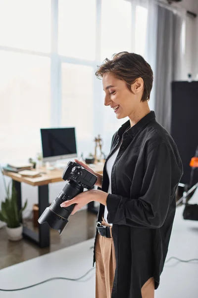 Cheerful female photographer in casual outfit with camera in her hands smiling and looking at photos — Stock Photo