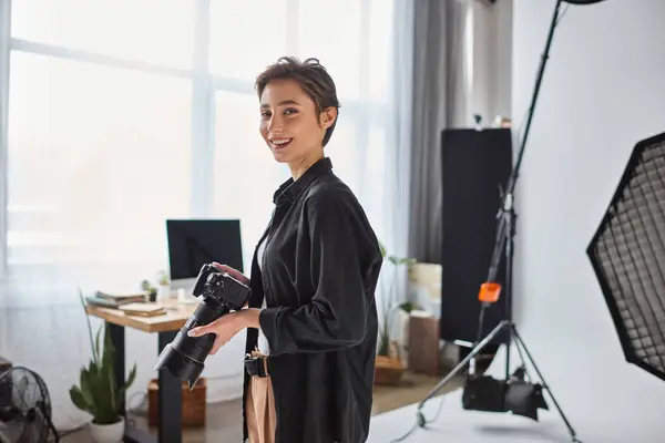 Glückliche junge Fotografin mit kurzen Haaren posiert mit ihrer Kamera und lächelt fröhlich — Stockfoto
