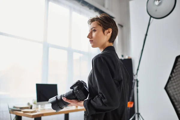 Attractive young female photographer in everyday clothes posing in her studio and looking away — Stock Photo